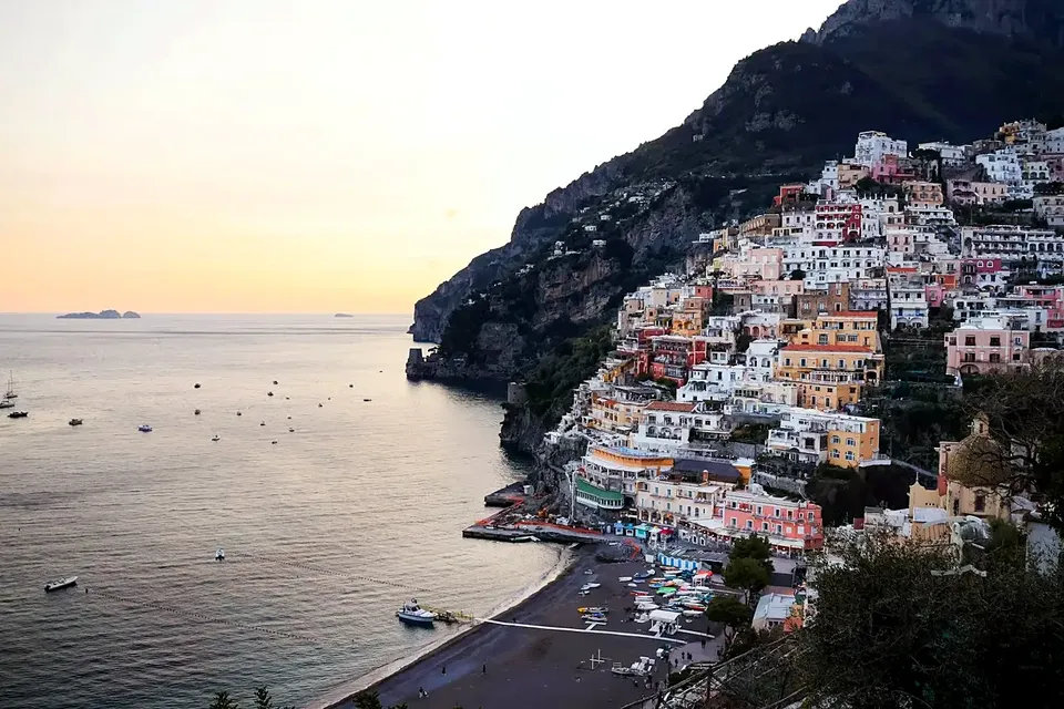 Blick auf Positano vom Meer aus: pastellfarbene Häuser steigen stufenförmig den Hügel hinauf, davor liegen die Fähren vor der Spiaggia Grande