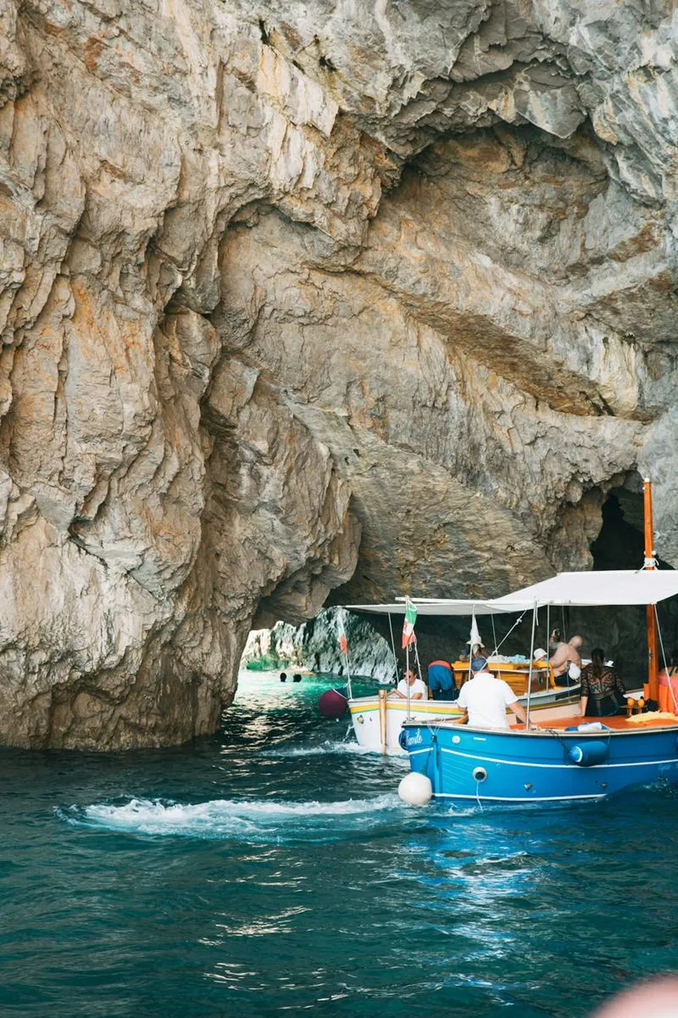 Boot entlang der Kalkfelsen von Capri mit den Faraglioni im Hintergrund und tiefblauem Meer