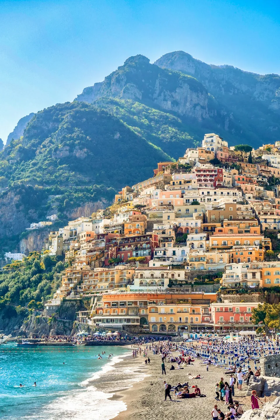 Ansteigende Gasse in Positano mit Boutiquen, bunten leichten Kleidern im Freien und Blick auf pastellfarbene Häuser in Richtung Meer